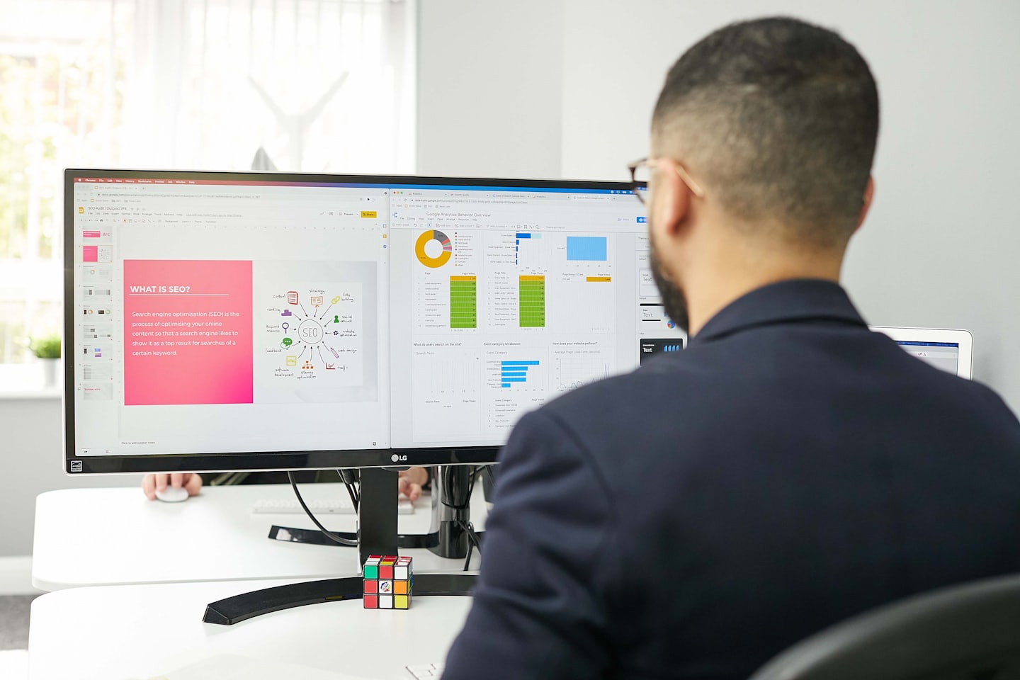Hombre trabajando en monitores de computadora duales que muestran SEO y análisis.