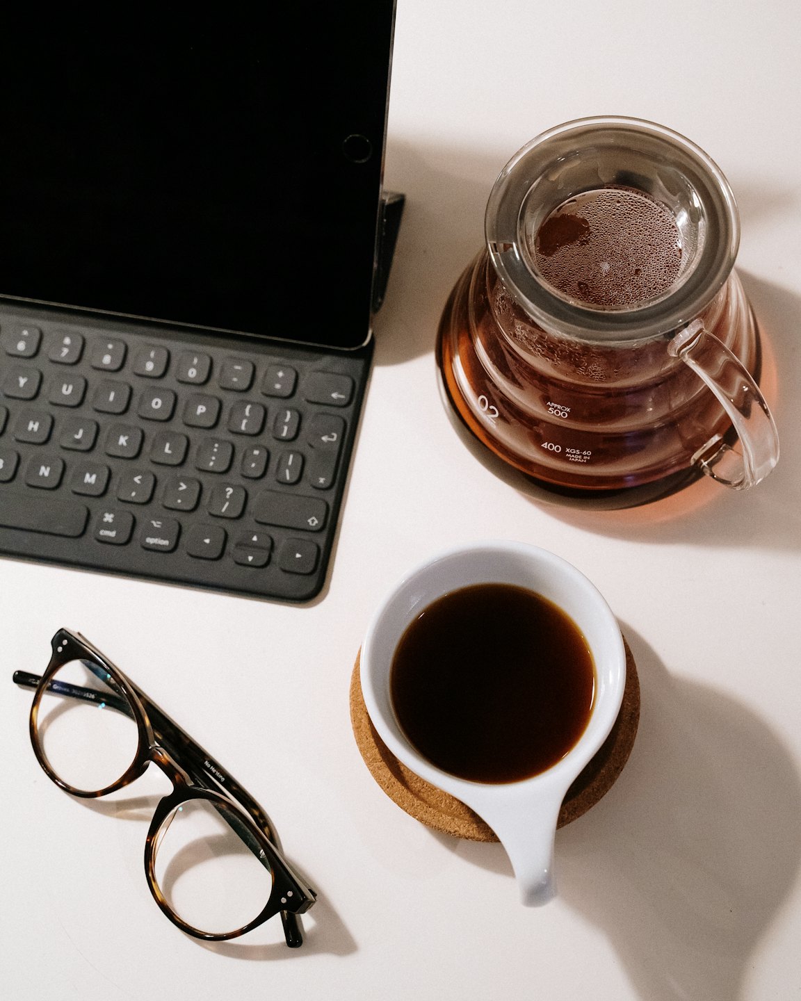 Una tableta con teclado, café y gafas sobre un escritorio.